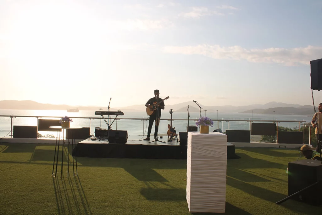 Musician silhouetted against sunset and harbour on the lawn area at Nambawan Super Plaza